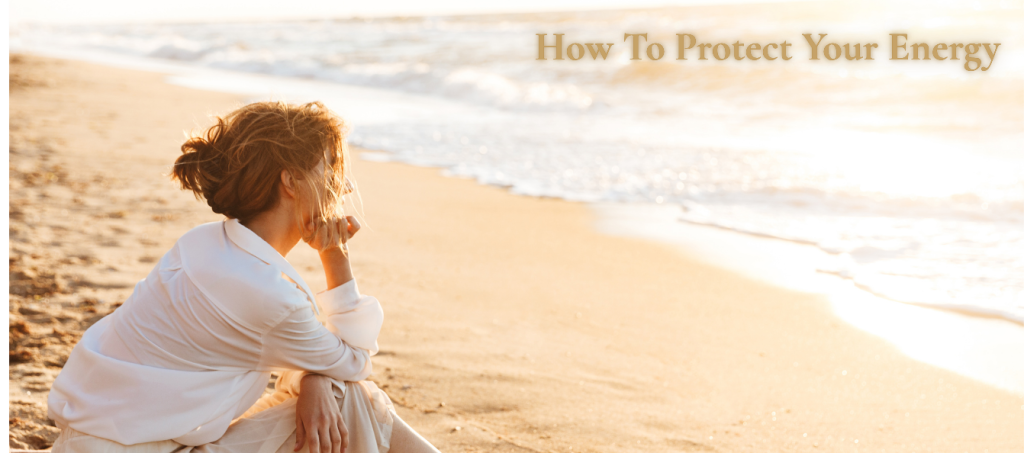Woman sitting peacefully by the sea, taking time to protect her energy and reconnect with herself.